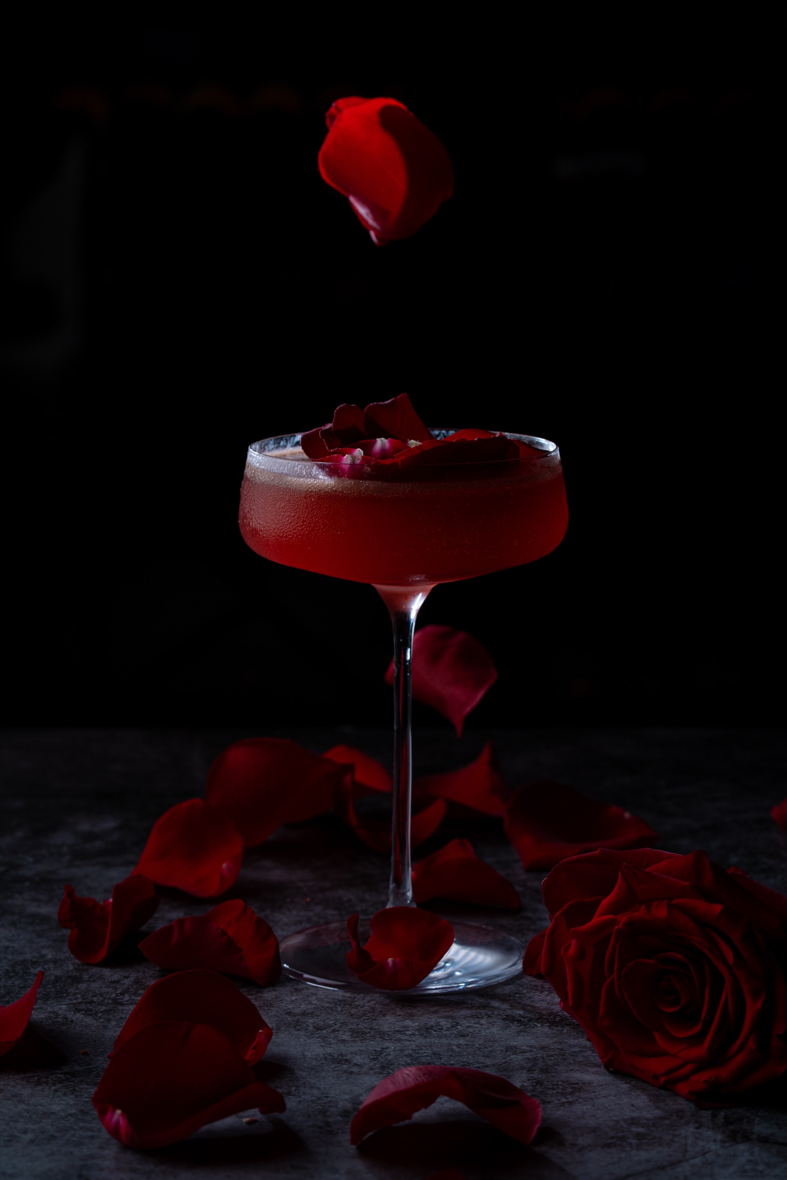 Red cocktail surrounded by rose petals
